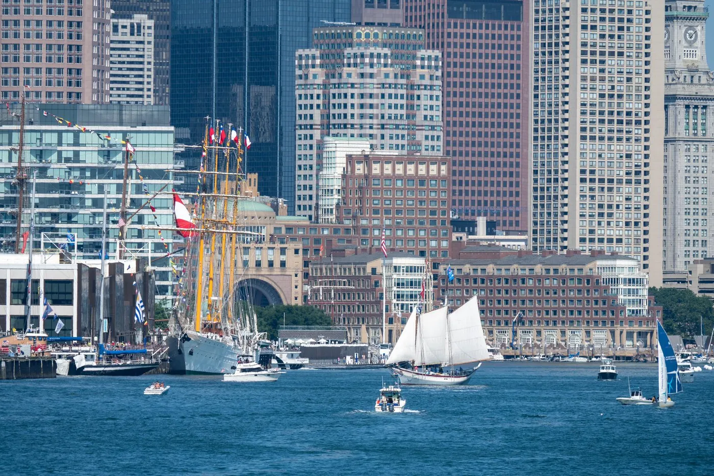 Sailboats and tall ships on Boston Harbor with the downtown skyline behind